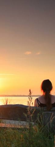 a seated women looking across the sea as the sunrises