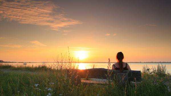 a seated women looking across the sea as the sunrises